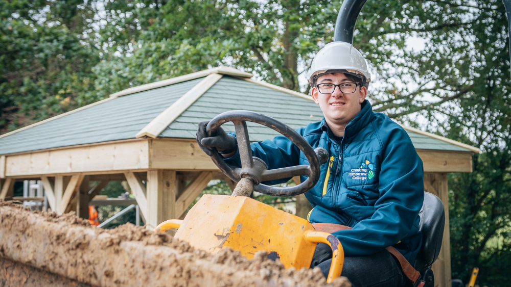 A student wearing Creating Tomorrow College uniform and safety gear driving a yellow bulldozer at an outdoor building site