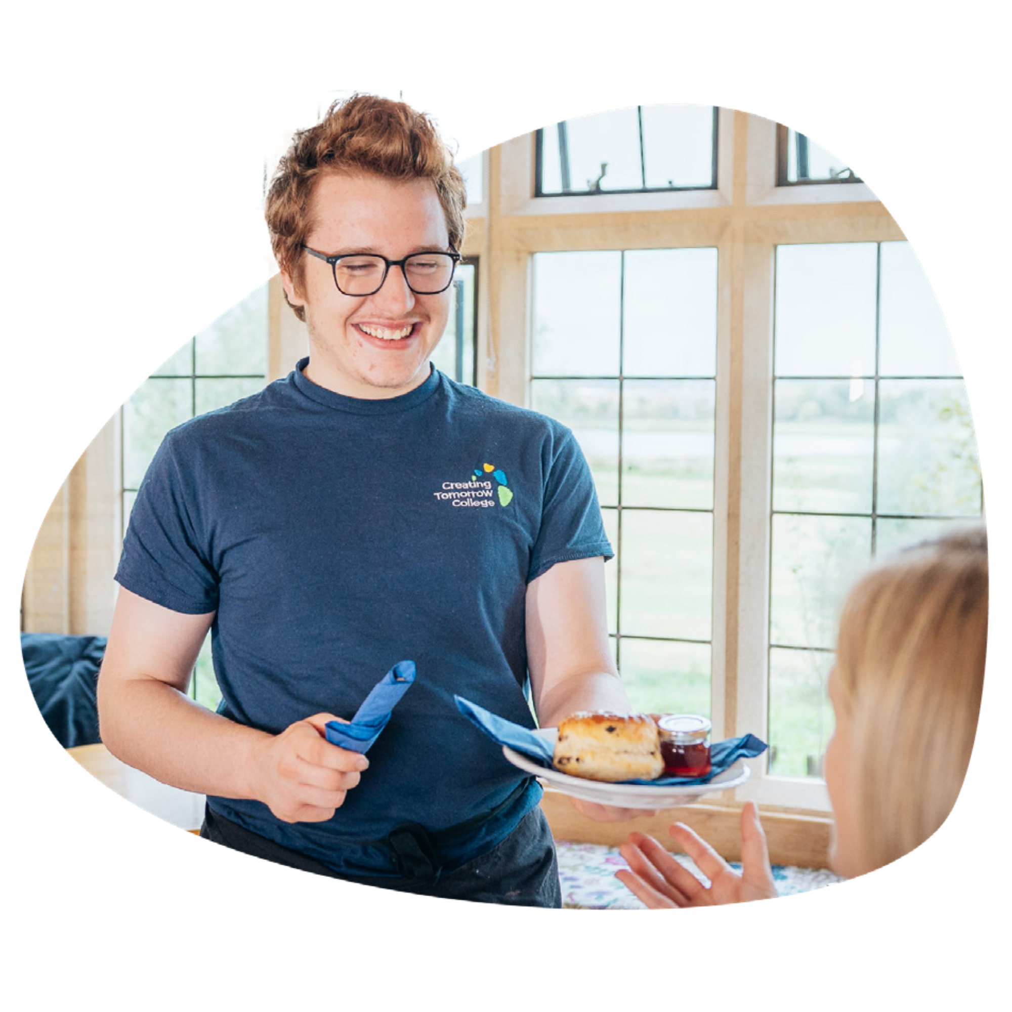 A smiling Creating Tomorrow College learner holding a plate with pastry on it, as if serving food to someone just out of frame.