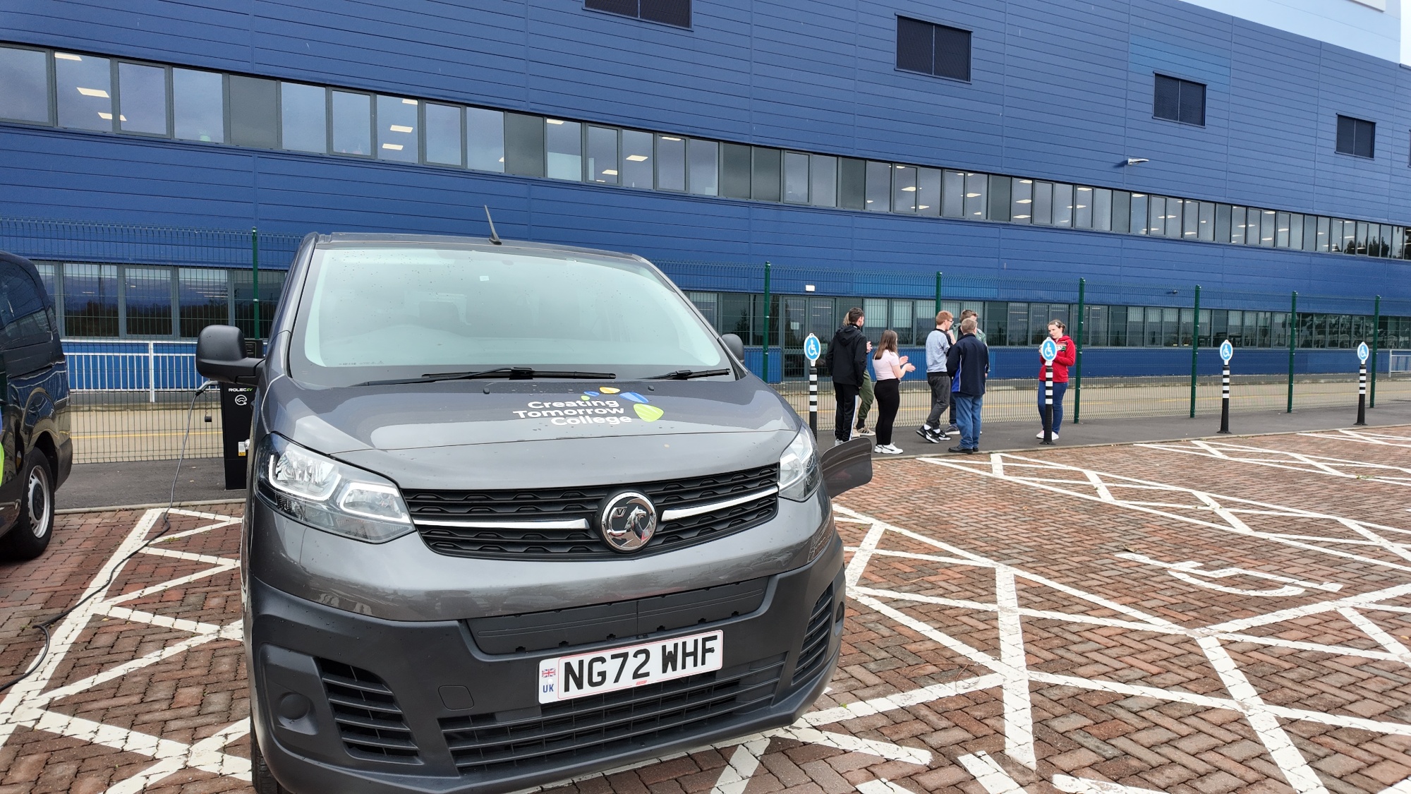 A brand-new grey minibus with Creating Tomorrow College logo on the front parked outside a modern Iron Mountain building