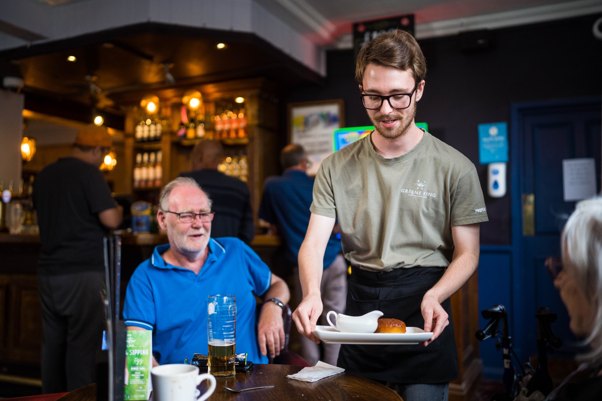 Photo of a student serving food to a customer in a bar.