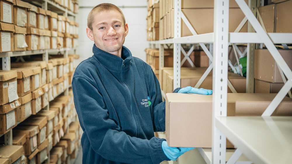 Creating Tomorrow College learner holding a box in a warehouse environment during a work experience wearing a Creating Tomorrow College uniform