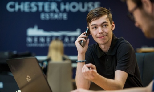 A learner sitting at a desk in an office holding a phone to his ear and smiling, a laptop is open in front of him