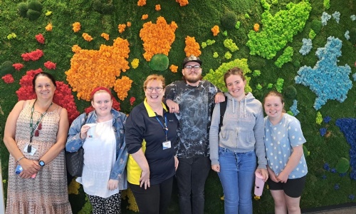 Picture of Alice Mullan with a group of students at Iron Mountain campus in front of a living moss wall 